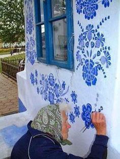 a man painting the side of a building with blue and white flowers on it's wall