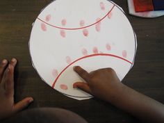 a child's hand is pointing at a paper plate with a baseball on it