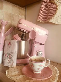 a pink coffee maker sitting on top of a counter next to a cup and saucer