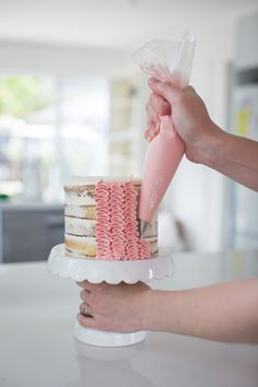 a person is decorating a cake with pink icing on a white table top