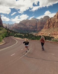 two people riding skateboards down the middle of a road in front of some mountains