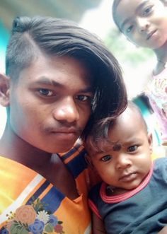 a man holding a baby next to two other children in front of him and looking at the camera