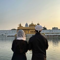 two people standing in front of a body of water with a building in the background