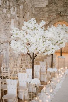 an aisle lined with chairs and tables covered in white flowered centerpieces for a wedding