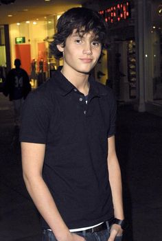 a young man standing in front of a building at night with his hands in his pockets