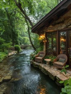 two wicker chairs sit on the edge of a small stream in front of a cabin