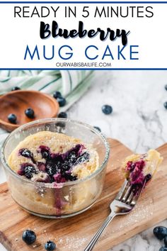 a blueberry mug cake in a glass bowl on a cutting board with a fork