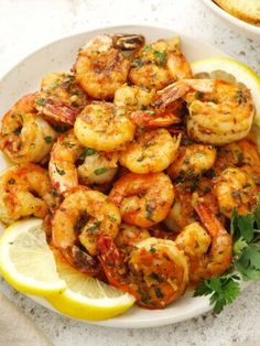 a white plate topped with shrimp next to lemon wedges and garnished with parsley