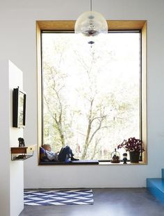 a person sitting on a window sill in front of a large window with a tree outside