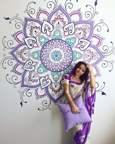 a woman standing in front of a wall with a purple and white flower design on it