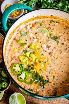 a large pot filled with mexican chicken soup surrounded by cilantro, jalapenos and limes