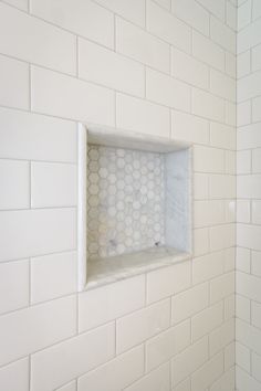 a white bathroom with hexagonal tiles on the wall and shelves in the corner