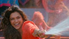 a woman in an orange shirt is spraying water on her face and smiling at the camera