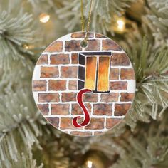 a christmas ornament hanging from a tree with a brick wall and red letter s on it