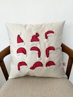 a white pillow with red santa hats on it sitting on top of a wooden chair