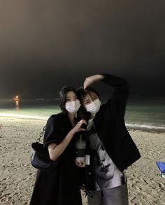 two people standing on the beach with masks covering their faces and one person taking a selfie