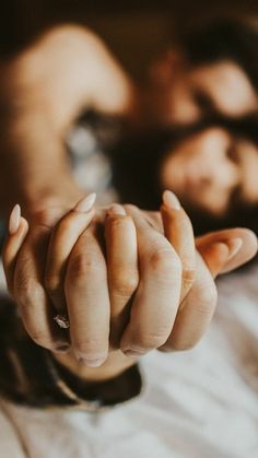 two people laying on a bed with one holding the other's hand in front of them