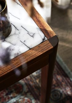 a marble top table with a wooden base and metal vase sitting on it's side