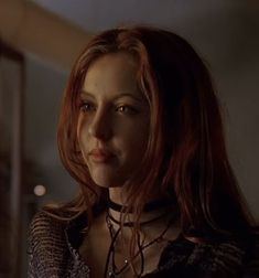 a woman with long red hair wearing a necklace and looking at something in the distance