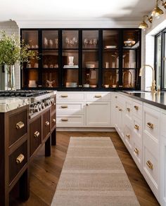 a kitchen with white cabinets and wooden floors, gold pulls on the doors, an area rug in front of the stove