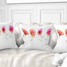 three pillows with flowers on them sitting on a white couch in front of a wall