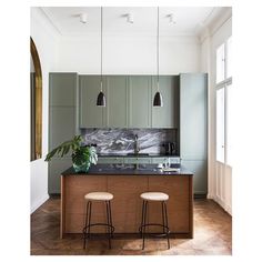 two stools sit in front of a kitchen island with marble counter tops and green cabinets