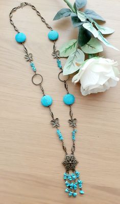 a necklace with turquoise beads and flowers on a wooden table next to a white flower