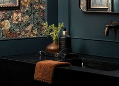 a bathroom with green walls and floral wallpaper, black countertop sink and gold faucet