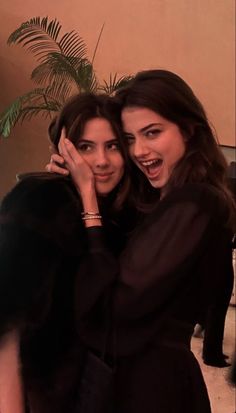 two young women hugging each other in front of a plant and potted palm tree