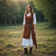 a woman wearing a brown and white dress standing in the grass with trees behind her