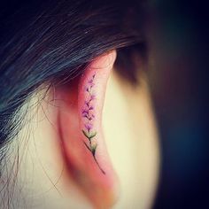 an ear tattoo with purple flowers on the inside of it and behind the ear is a pink flower