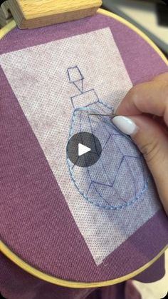 someone is stitching something on the back of a purple and white bag with a blue design