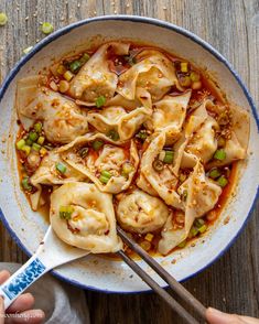 a white bowl filled with dumplings and sauce on top of a wooden table next to chopsticks