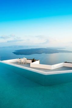 an outdoor swimming pool with chairs and tables on the edge in front of blue water