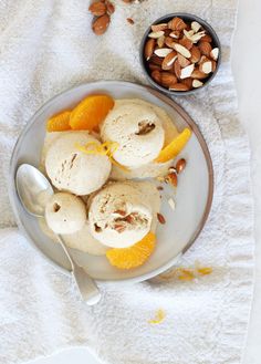 an orange gelato with almonds and orange slices on a plate next to a bowl of nuts