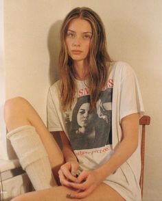 a woman sitting on top of a wooden chair next to a wall with her legs crossed