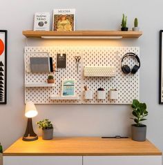 a desk with headphones, books and plants on it in front of a white wall