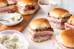 several sandwiches with different toppings are on a cutting board next to bowls of food