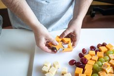 a person cutting up cheese and grapes on a cutting board