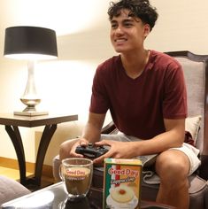 a young man sitting on a couch holding a game controller in front of a cup of coffee