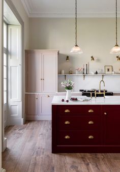 a kitchen with wooden floors and white walls, two lights hanging from the ceiling over the island