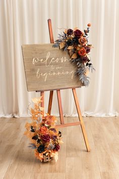 a welcome sign with flowers on it sitting in front of a white curtained backdrop