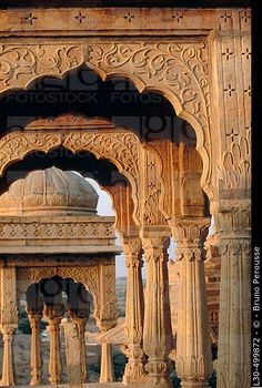 an intricately carved stone structure with pillars and arches in the middle of a desert area