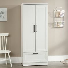 a white armoire next to a chair in a living room with beige walls and wood floors