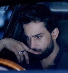 a man with a ring on his finger sitting in a car looking at the camera