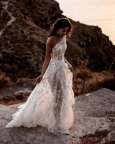 a woman in a white wedding dress walking on the beach at sunset with her back to the camera