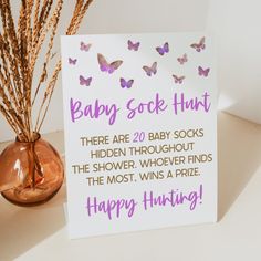 a baby sock hunt sign next to a vase filled with dry grass and purple butterflies