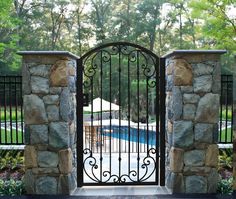 an iron gate is open to a pool in the back yard with stone walls and wrought iron gates