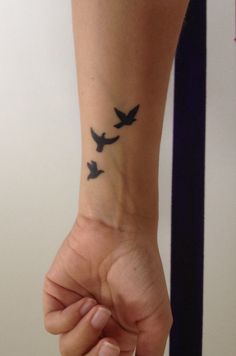 a woman's wrist tattoo with three birds flying in the sky on her left arm