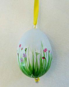 a glass ornament with grass and flowers painted on the outside, hanging from a yellow cord